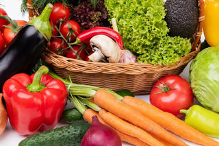 View of fresh garden vegetables including bell peppers, tomatoes, carrots, cucumbers, lettuce, and avocados in a woven basket.